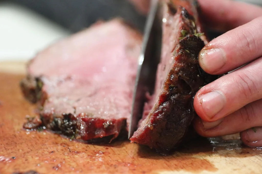 Hands cutting a beef chuck roast into cubes for stew