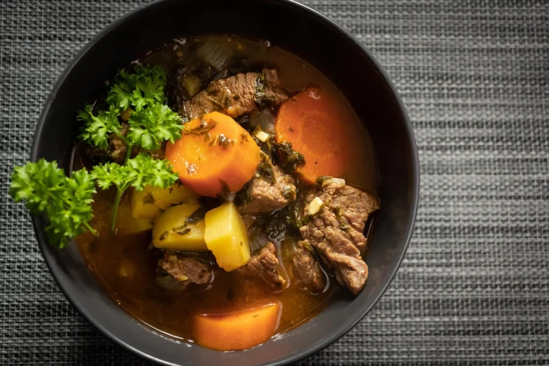 A bowl of finished beef stew with tender beef, carrots, and potatoes, ready to eat